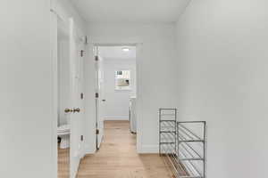 Corridor with washer / clothes dryer, light wood-style floors, baseboards, and an upstairs landing