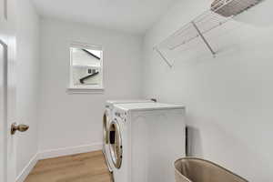 Laundry area featuring washer and clothes dryer, light wood finished floors, laundry area, and baseboards