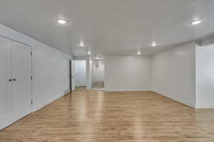 Finished basement with light wood-style flooring, a textured ceiling, visible vents, recessed lighting, and baseboards