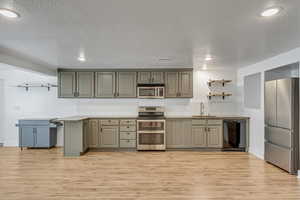 Kitchen featuring light wood finished floors, a sink, open shelves, and appliances with stainless steel finishes