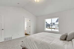 Carpeted bedroom with visible vents, baseboards, ensuite bathroom, and lofted ceiling