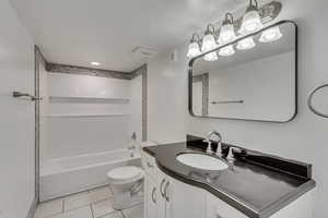 Full bath with a textured ceiling, vanity, tile patterned flooring,  shower combination, and toilet