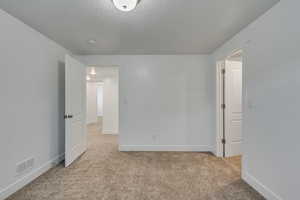 Empty room with visible vents, baseboards, light colored carpet, and a textured ceiling