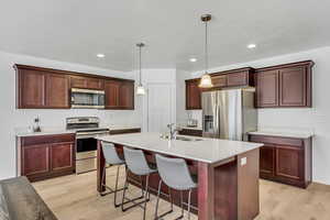 Kitchen with light wood-type flooring, recessed lighting, light countertops, stainless steel appliances, and a sink