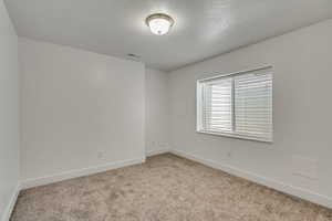 Spare room with light carpet, visible vents, baseboards, and a textured ceiling