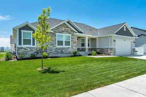 Craftsman house featuring concrete driveway, stone siding, board and batten siding, a front lawn, and an attached garage