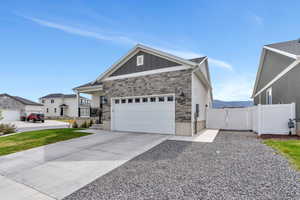 View of front of home featuring concrete driveway, board and batten siding, stone siding, an attached garage, and fence