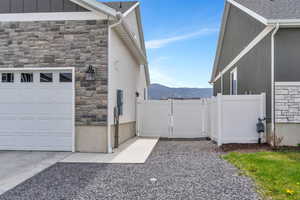 View of home's exterior with stucco siding, a gate, fence, stone siding, and a mountain view
