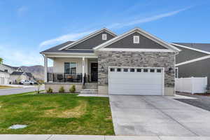 Craftsman-style home featuring a front lawn, covered porch, stone siding, board and batten siding, and an attached garage