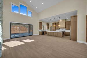 Unfurnished living room with high vaulted ceiling, light wood-style flooring, and baseboards