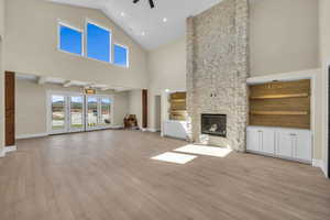 Unfurnished living room with wood finished floors, ceiling fan, a fireplace, baseboards, and high vaulted ceiling