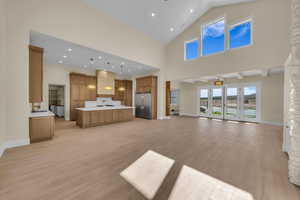 Unfurnished living room with light wood-style floors, plenty of natural light, high vaulted ceiling, and baseboards