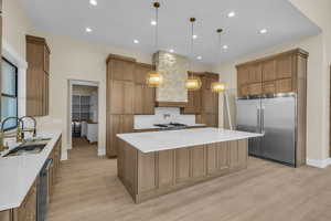 Kitchen featuring a spacious island, appliances with stainless steel finishes, backsplash, light wood finished floors, and a sink