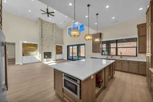 Kitchen with stainless steel microwave, a sink, light wood-style floors, a fireplace, and high vaulted ceiling