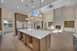 Kitchen with high vaulted ceiling, built in refrigerator, a kitchen island, light wood-style flooring, and ceiling fan with notable chandelier