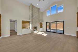 Unfurnished living room featuring a fireplace, ceiling fan, high vaulted ceiling, baseboards, and wood finished floors