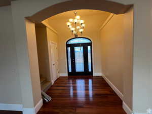 Foyer entrance featuring arched walkways, an inviting chandelier, stairs, and wood finished floors