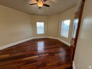 Spare room featuring baseboards, ceiling fan, a wealth of natural light, and dark wood-type flooring