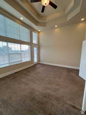 Empty room featuring dark colored carpet, a raised ceiling, baseboards, recessed lighting, and a ceiling fan