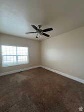 Empty room featuring a ceiling fan, visible vents, dark colored carpet, and baseboards