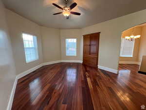 Unfurnished room with dark wood-style floors, ceiling fan with notable chandelier, baseboards, and plenty of natural light