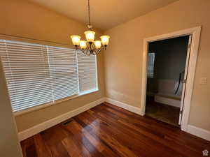 Unfurnished dining area with dark wood-style floors, an inviting chandelier, visible vents, and baseboards