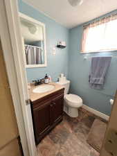 Full bath with toilet, a textured ceiling, stone finish floor, and vanity