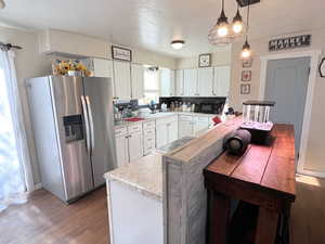 Kitchen with stainless steel fridge, black microwave, light countertops, white cabinets, and wood finished floors