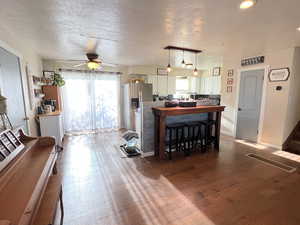 Kitchen with ceiling fan, decorative light fixtures, a textured ceiling, white cabinets, and wood finished floors