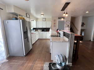 Kitchen with dark wood-style floors, stainless steel refrigerator with ice dispenser, white cabinetry, a peninsula, and light countertops