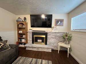 Living area featuring a fireplace, wooden walls, a wainscoted wall, a textured ceiling, and wood finished floors