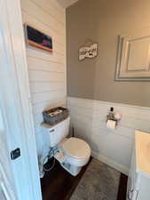 Half bath with wood walls, vanity, toilet, and wainscoting