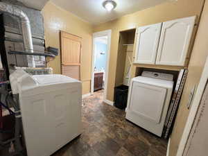 Laundry room featuring washing machine and dryer, cabinet space, stone finish floor, and baseboards
