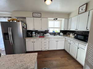 Kitchen featuring a sink, dark wood-style flooring, black microwave, stainless steel refrigerator with ice dispenser, and white cabinets