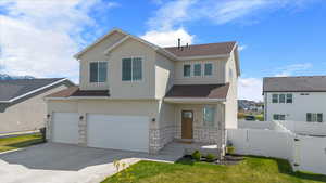 View of front of property featuring a shingled roof, stone siding, concrete driveway, stucco siding, and fence
