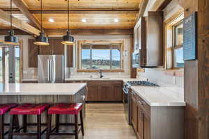 Kitchen with appliances with stainless steel finishes, wood ceiling, light countertops, and a sink