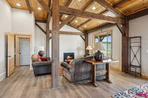 Living room featuring wood ceiling, beam ceiling, light wood-type flooring, and a lit fireplace