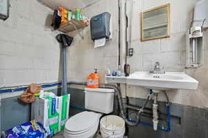 Bathroom featuring toilet, a sink, and concrete block wall