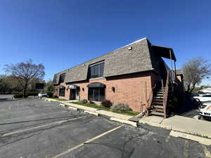 Exterior space featuring brick siding, a shingled roof, uncovered parking, and mansard roof