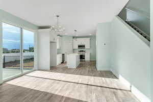 Kitchen featuring light wood-style flooring, stainless steel appliances, a kitchen island, white cabinetry, and a notable chandelier