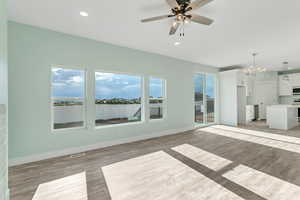 Unfurnished living room featuring light wood-style floors, baseboards, visible vents, and ceiling fan with notable chandelier