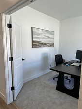 Carpeted office featuring a textured ceiling and baseboards