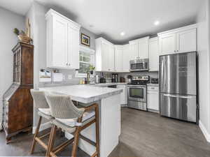 Kitchen featuring stainless steel appliances, a kitchen bar, white cabinetry, a peninsula, and light countertops