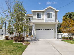 Traditional-style home with a porch, a front yard, concrete driveway, an attached garage, and fence