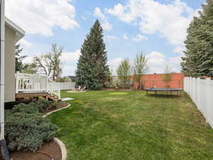 View of yard with a wooden deck, a fenced backyard, an outdoor fire pit, and a trampoline