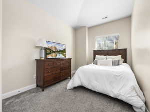 Carpeted bedroom with visible vents, vaulted ceiling, and baseboards