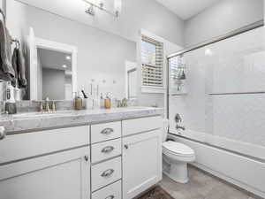Bathroom featuring double vanity, enclosed tub / shower combo, toilet, and a sink