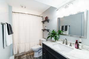 Full bathroom with wood finished floors, toilet, visible vents, and vanity