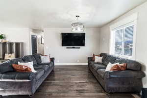 Living room with dark wood-style flooring, a notable chandelier, and baseboards