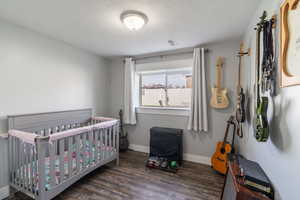 Bedroom with wood finished floors, a crib, baseboards, visible vents, and a textured ceiling